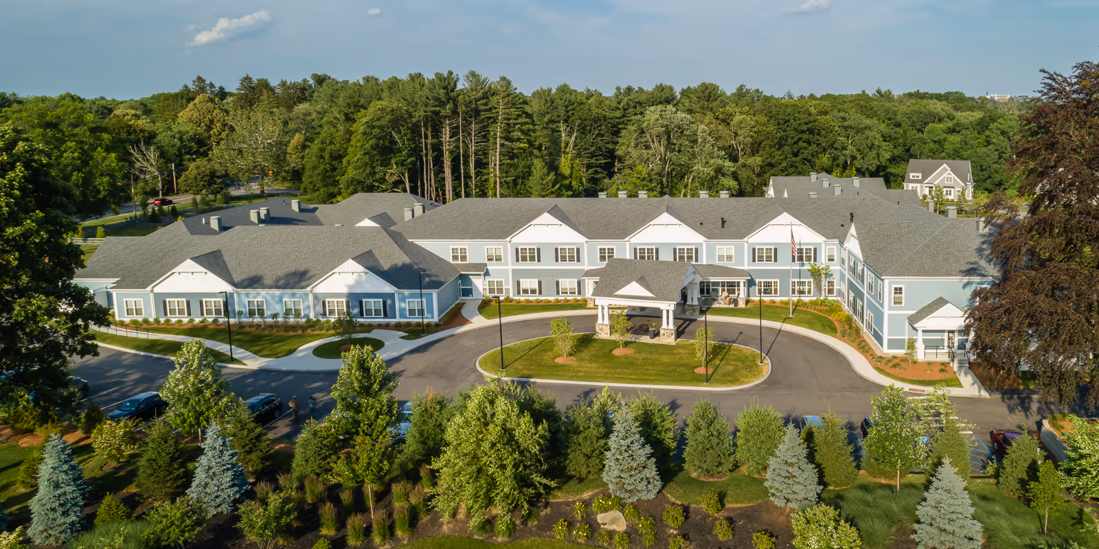 A sprawling senior living campus with a multi-wing building, circular driveway, and surrounding trees.