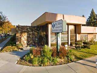 Exterior view of St. Edna Sub-Acute and Rehabilitation Center building with a sign displaying the facility name, surrounded by landscaped greenery and a sidewalk.