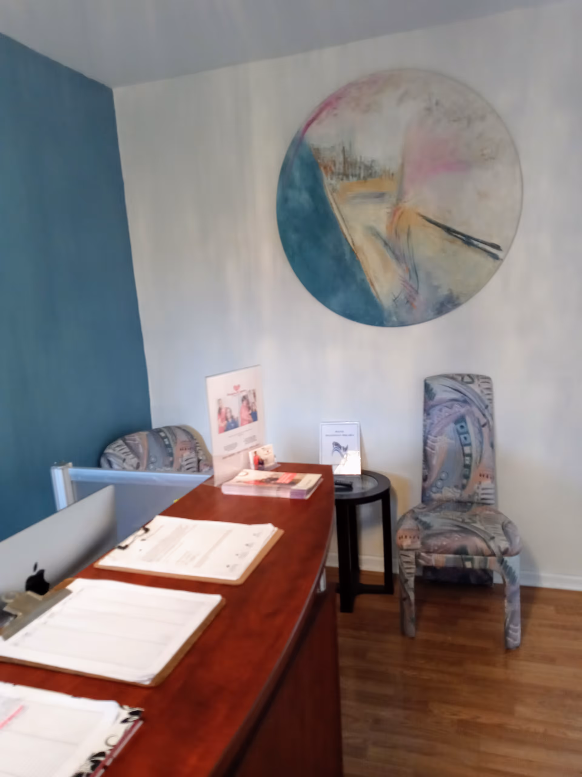 Reception desk in a small interior lobby with two patterned chairs and abstract wall art.