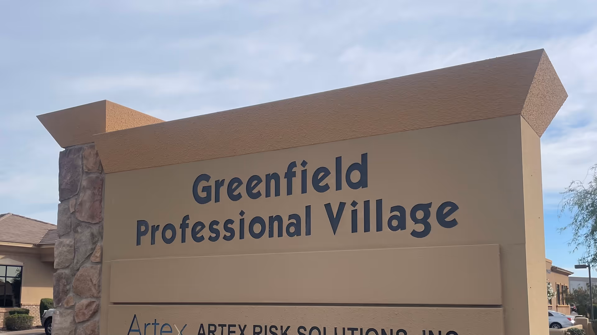 Exterior view of a large beige sign reading Greenfield Professional Village at the entrance.