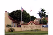 Exterior view of Spanish Meadows of Brownsville with entrance sign and flagpoles.