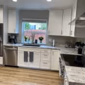 Bright kitchen with white cabinets, stainless appliances, a window, and herbs on the counter.