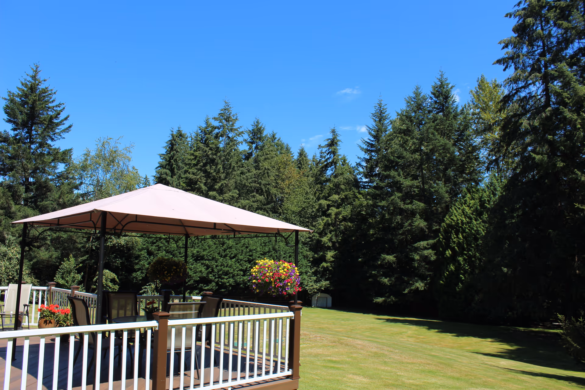 Outdoor wooden deck with beige canopy, seating, flower pots, and green lawn.