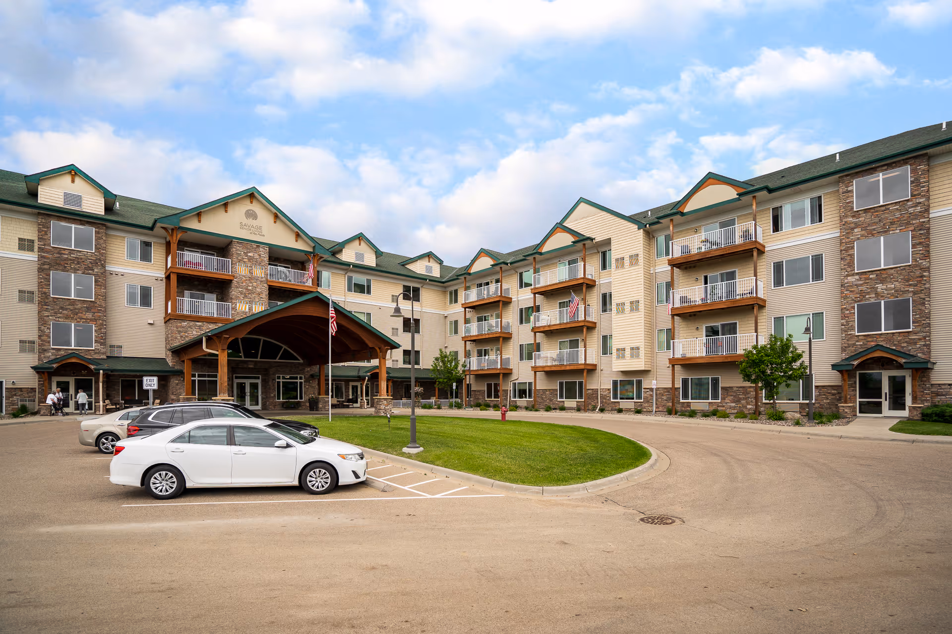 Exterior view of a multi-story senior living building with a covered entrance and parked cars
