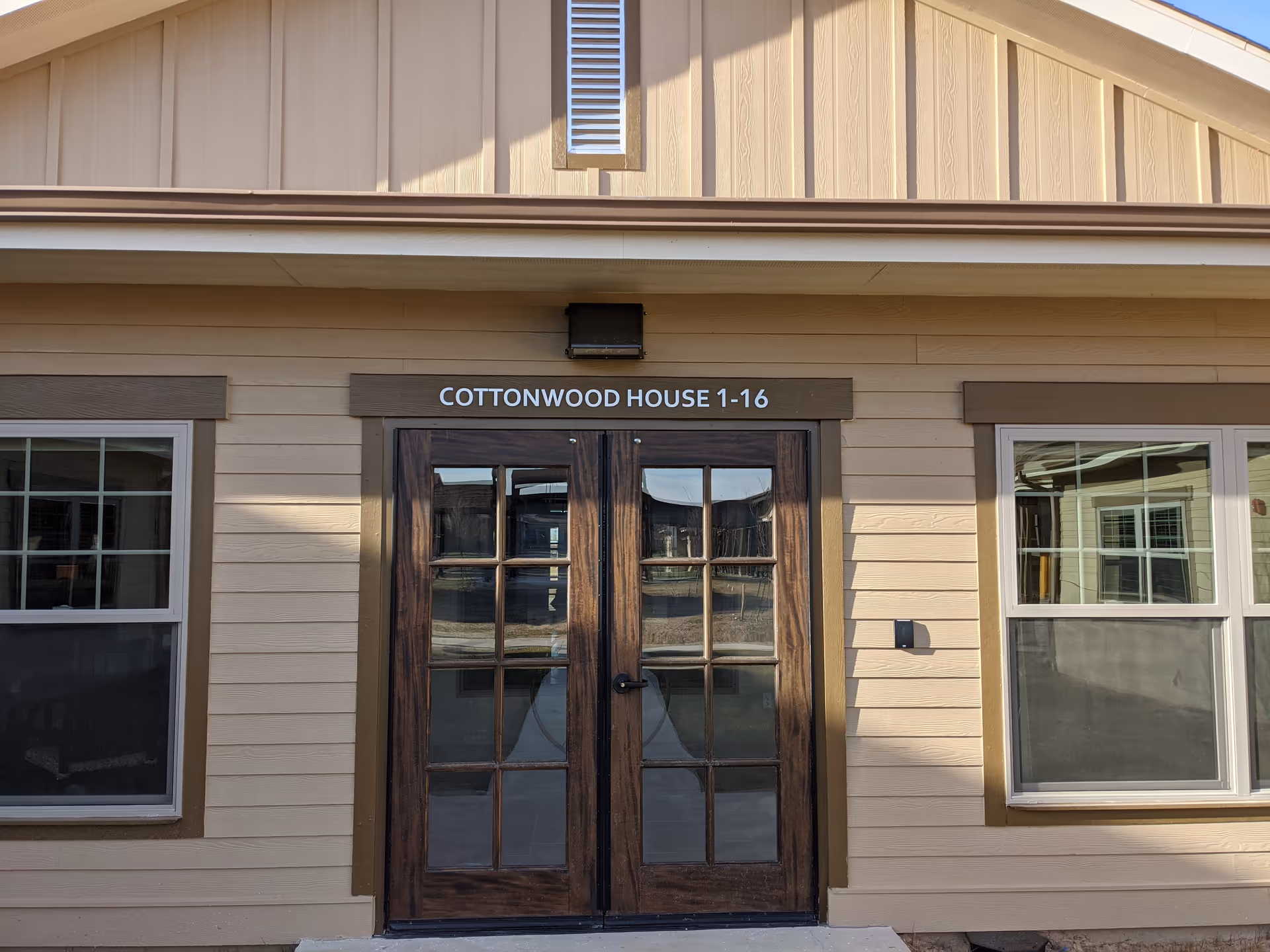 Tan facility exterior with wooden double doors and a Cottonwood House sign.