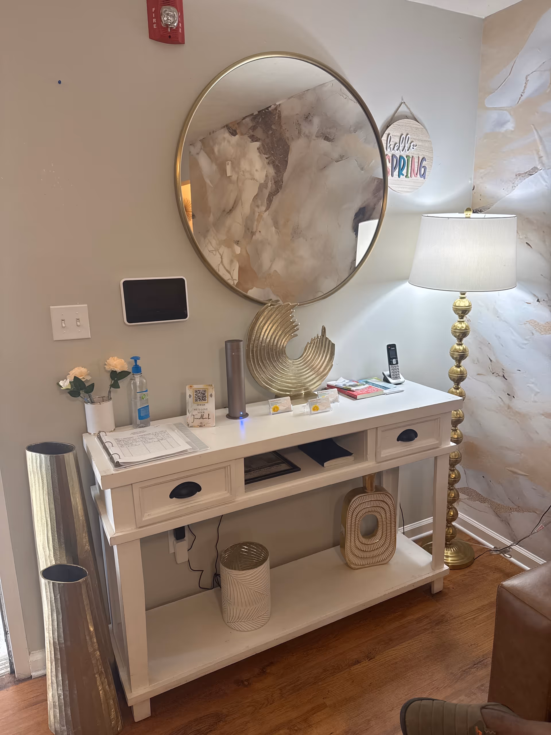 White console table with round mirror, lamp, and decorative items in a lobby.