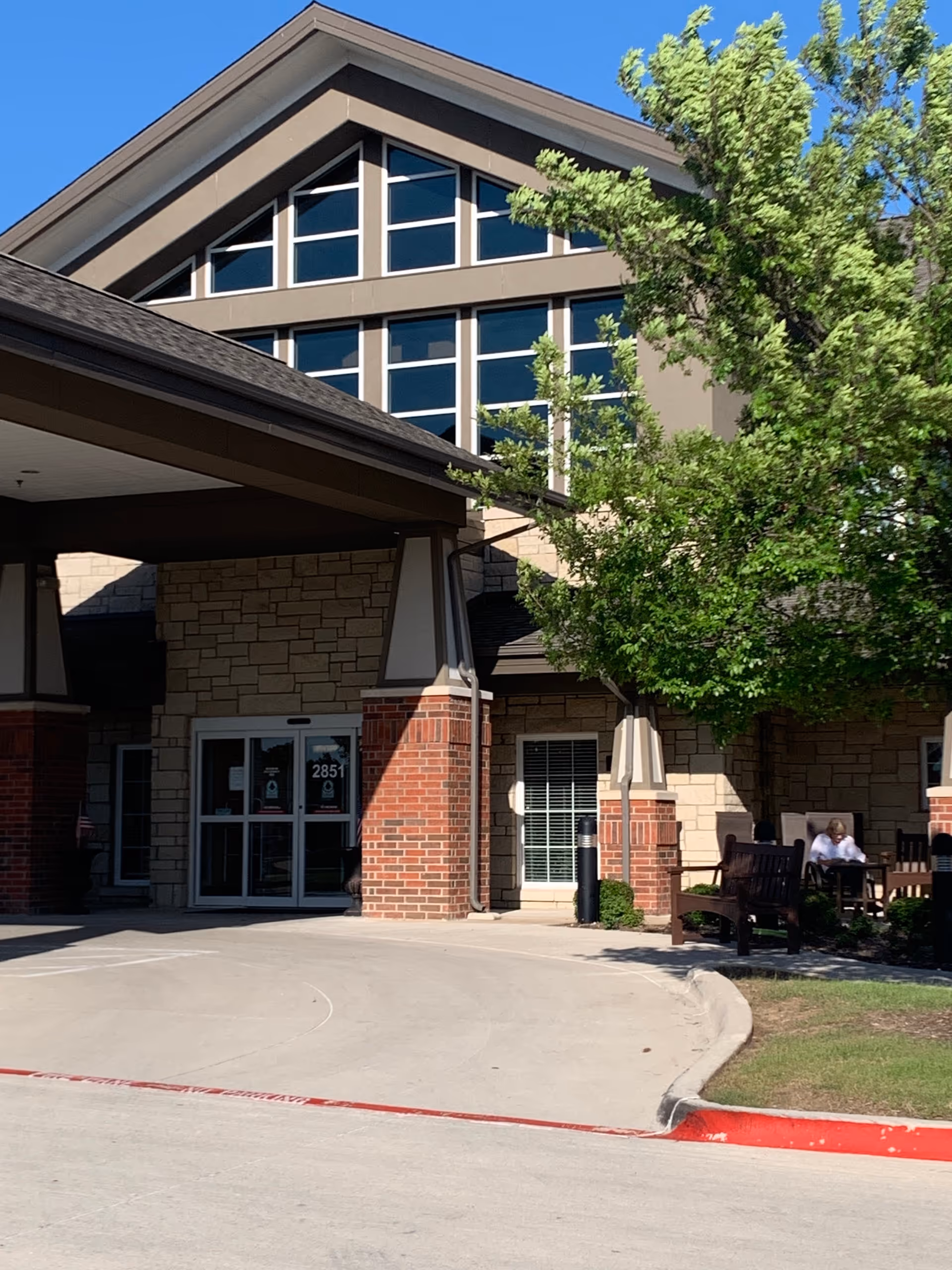 Front exterior of The Oxford Grand Assisted Living entrance with brick pillars and seating.