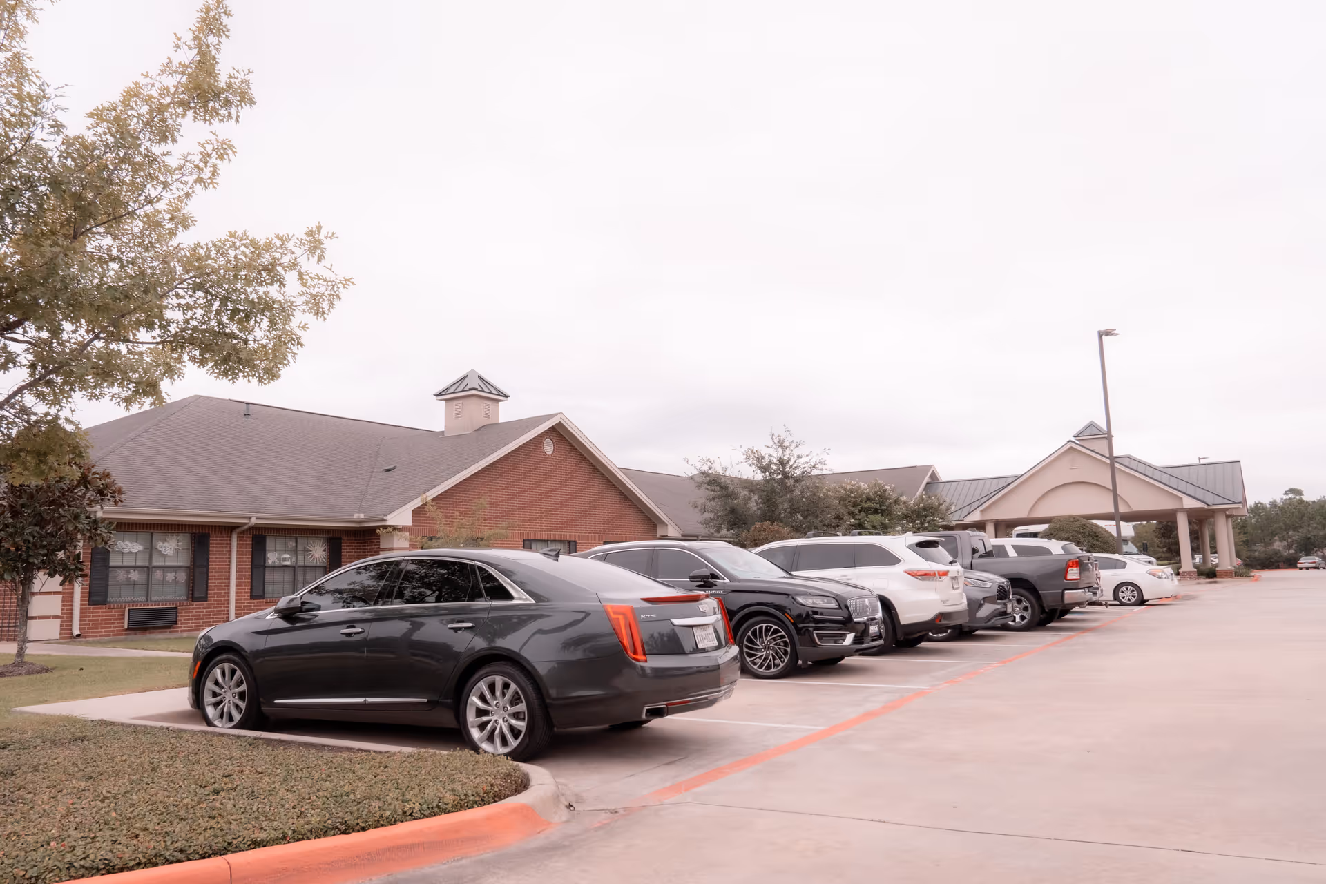 Row of parked cars in front of a single-story brick building with a covered entrance and landscaped grounds.