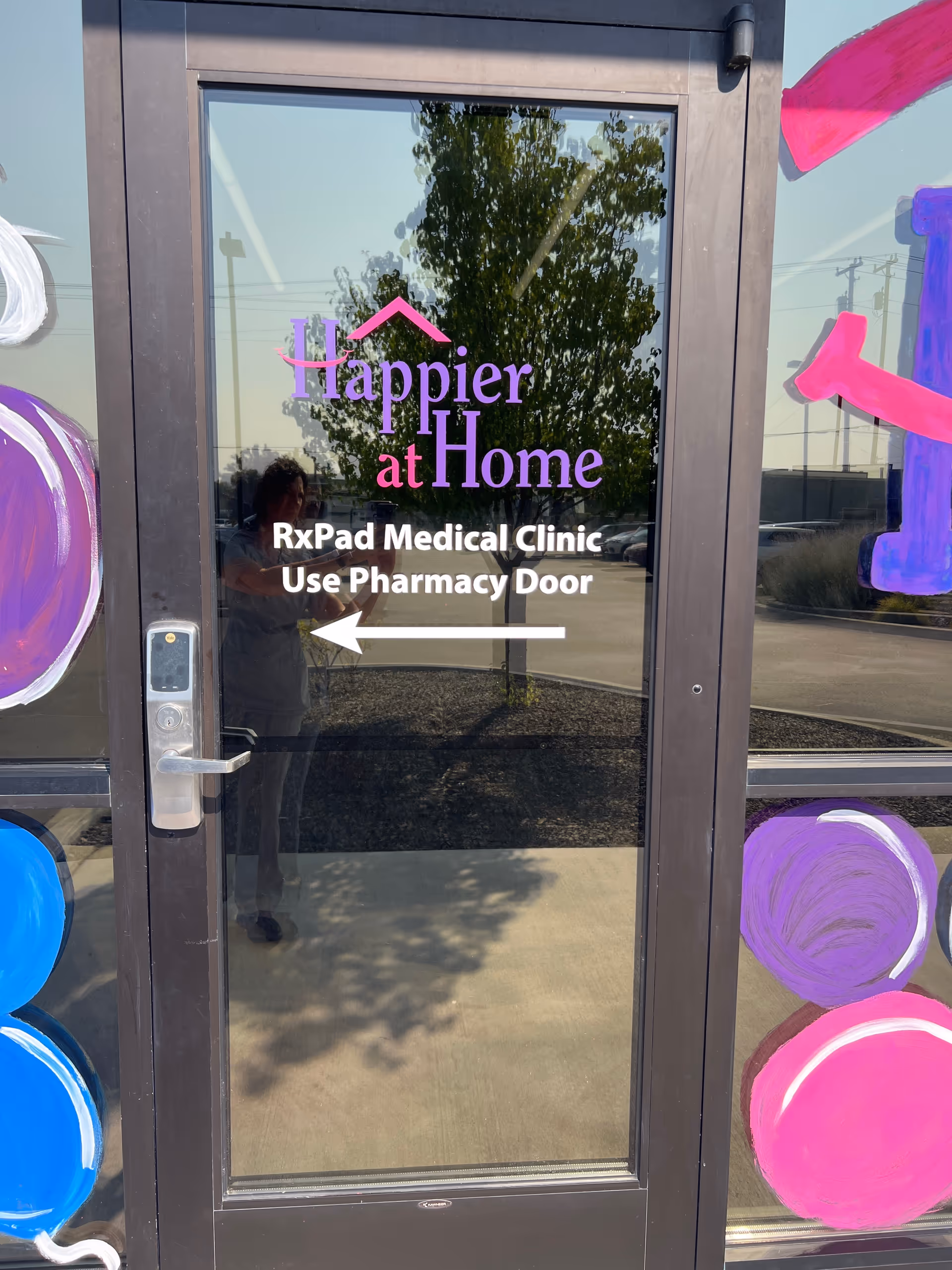 Glass door entrance with Happier at Home sign, RxPad Medical Clinic text, and colorful decorations.