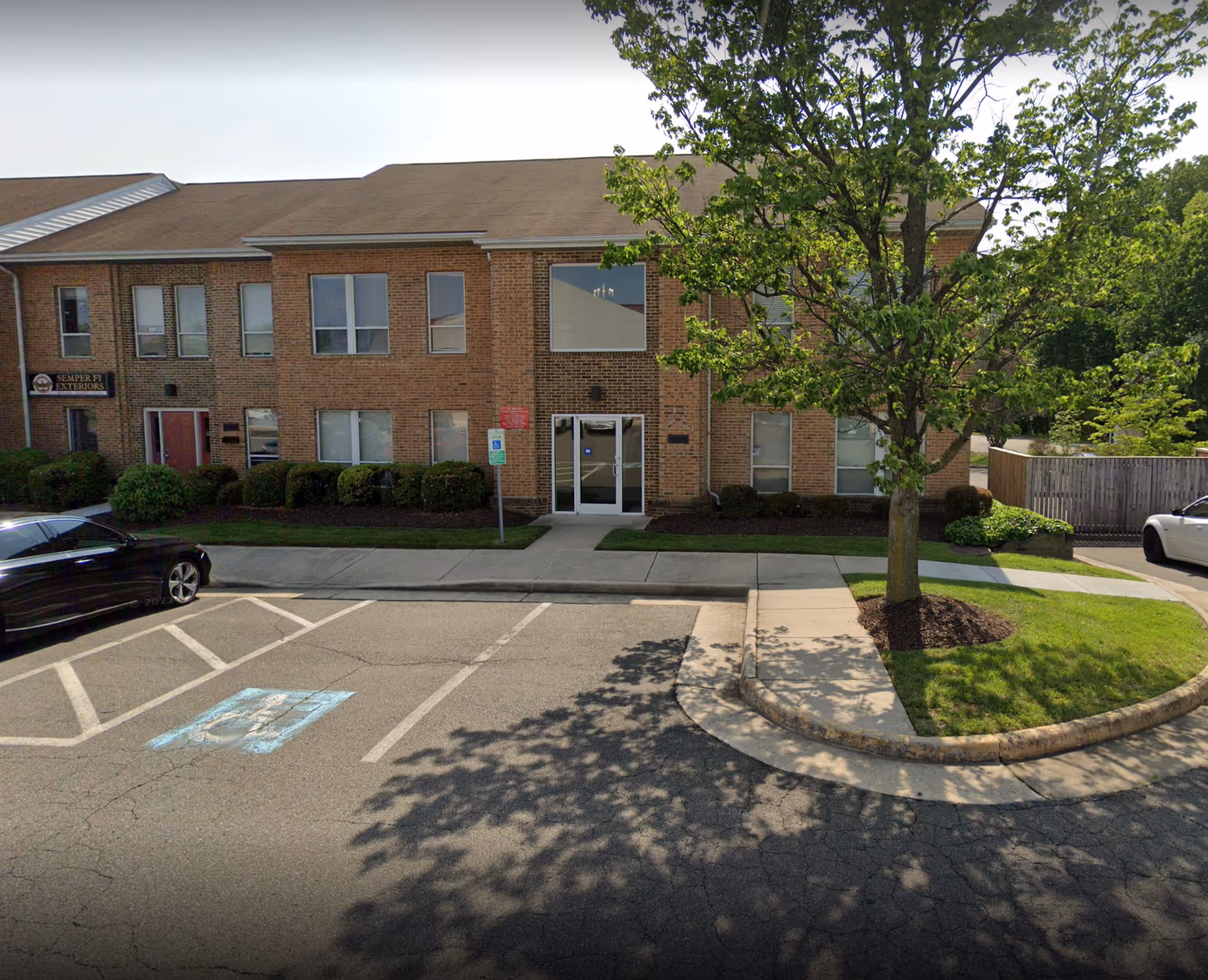 Brick senior living facility building with entrance, parking lot, and trees.