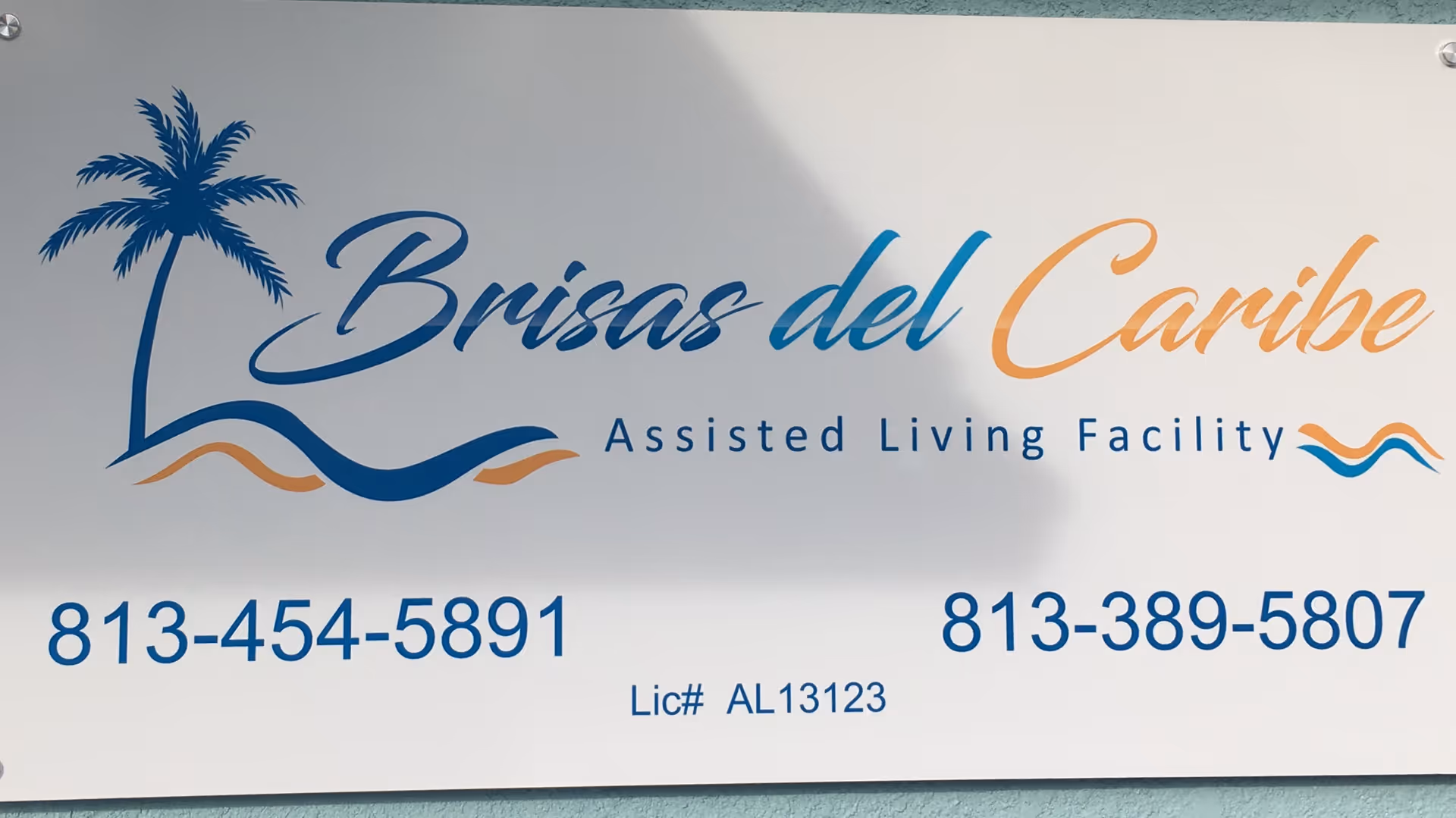 Sign reads Brisas del Caribe Assisted Living Facility with a palm tree graphic and phone numbers.