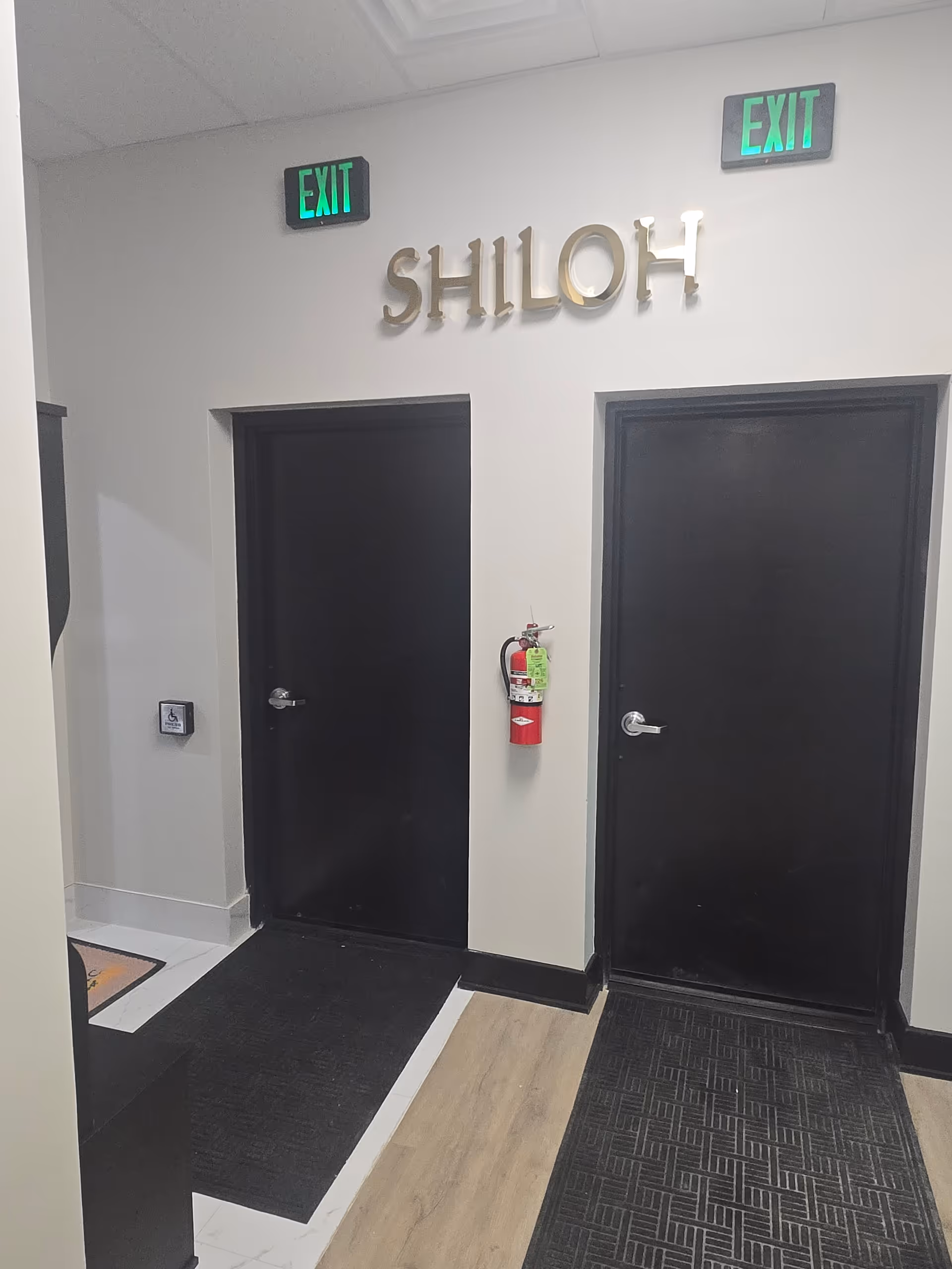 Interior hallway with two black doors, SHILOH sign, exit signs, and mounted fire extinguisher.