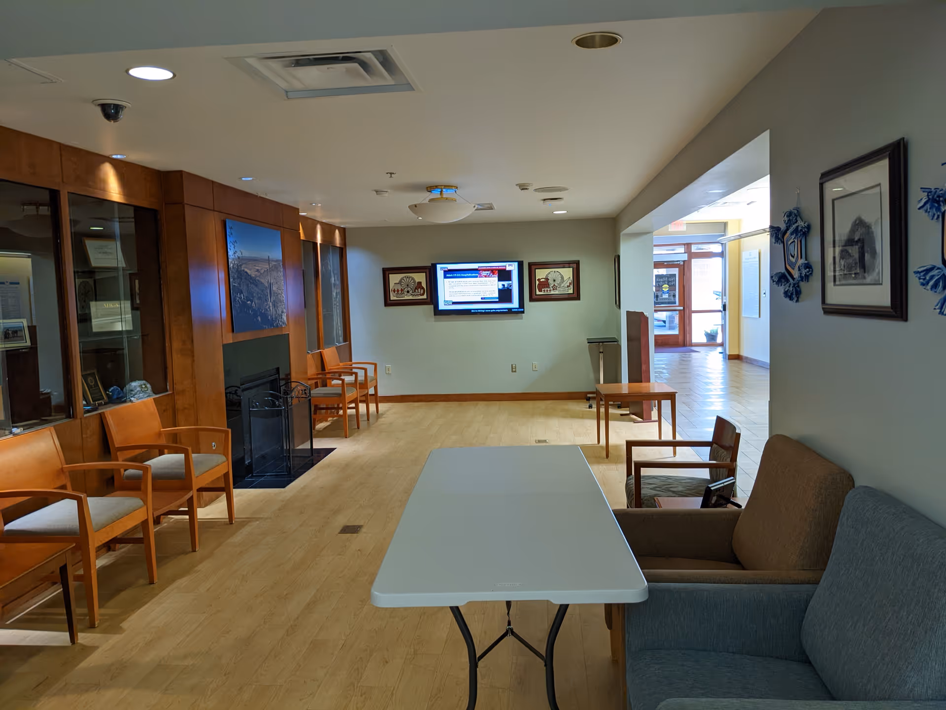 Empty lobby with wooden chairs, a sofa, and a rectangular table facing a TV.