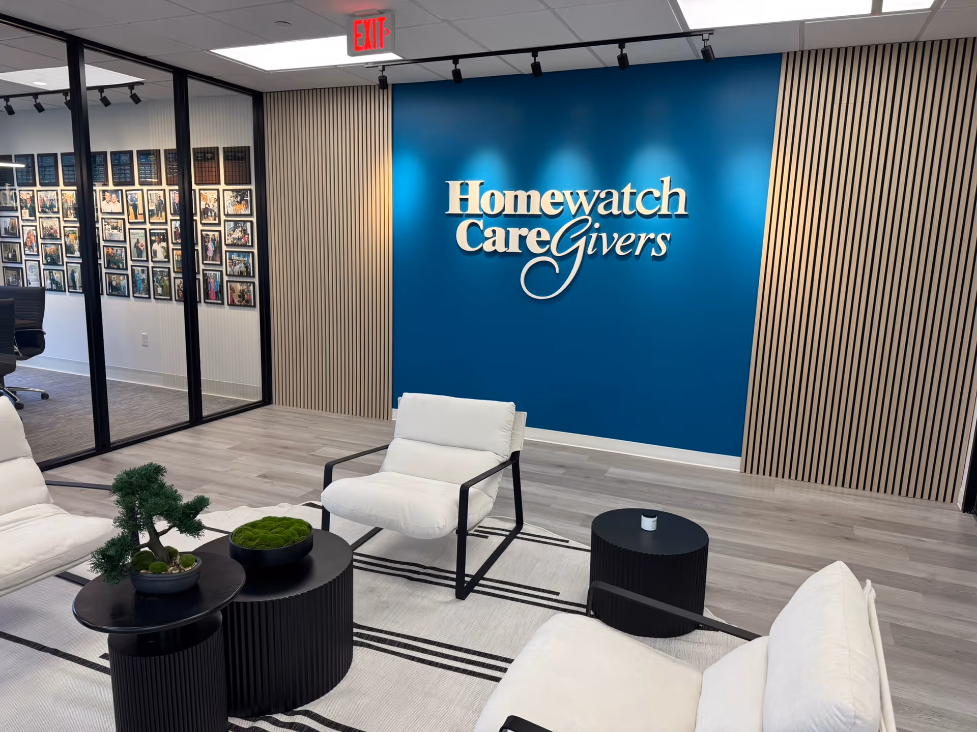 Modern lobby with blue branding wall, Homewatch CareGivers logo, and white seating.