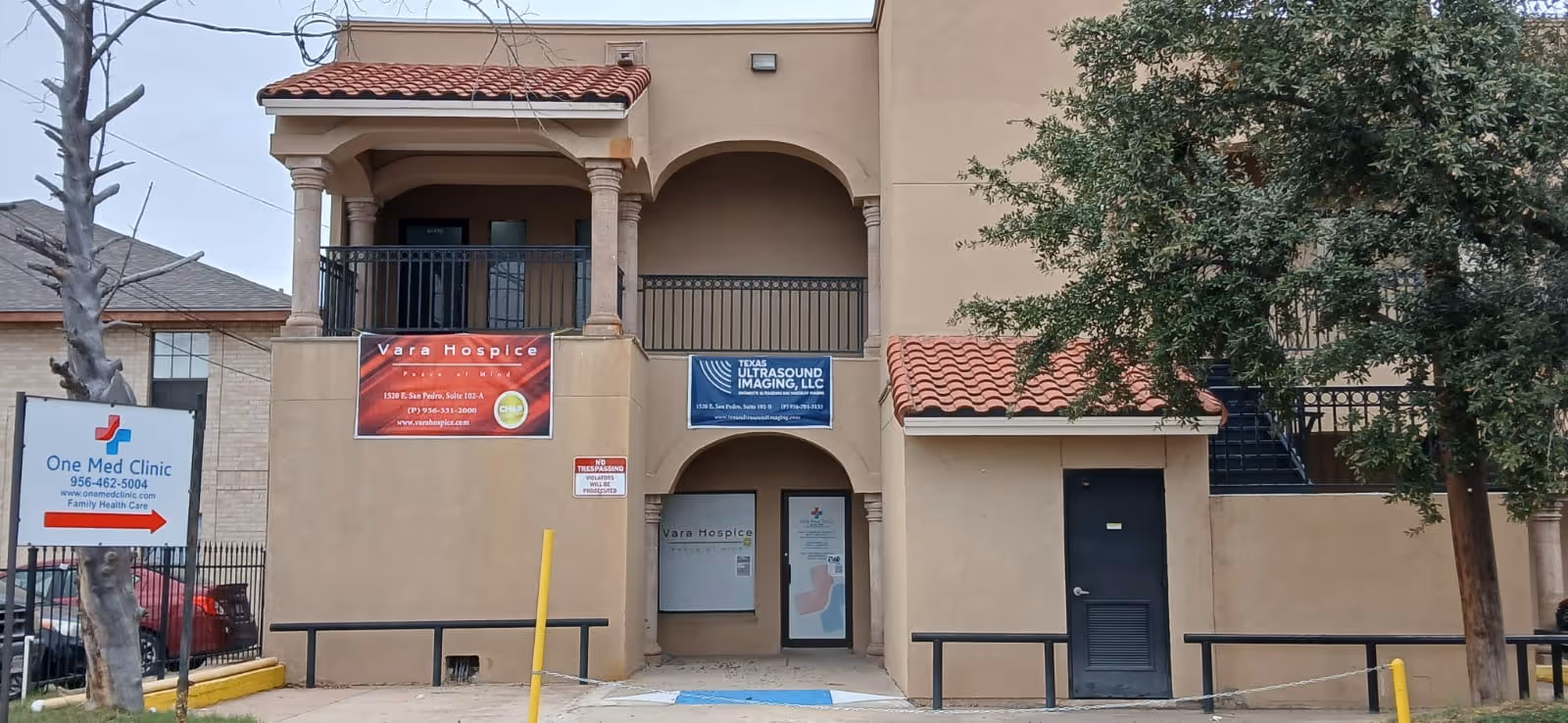 Two-story tan building facade with arches and Vara Hospice banners at the entrance.