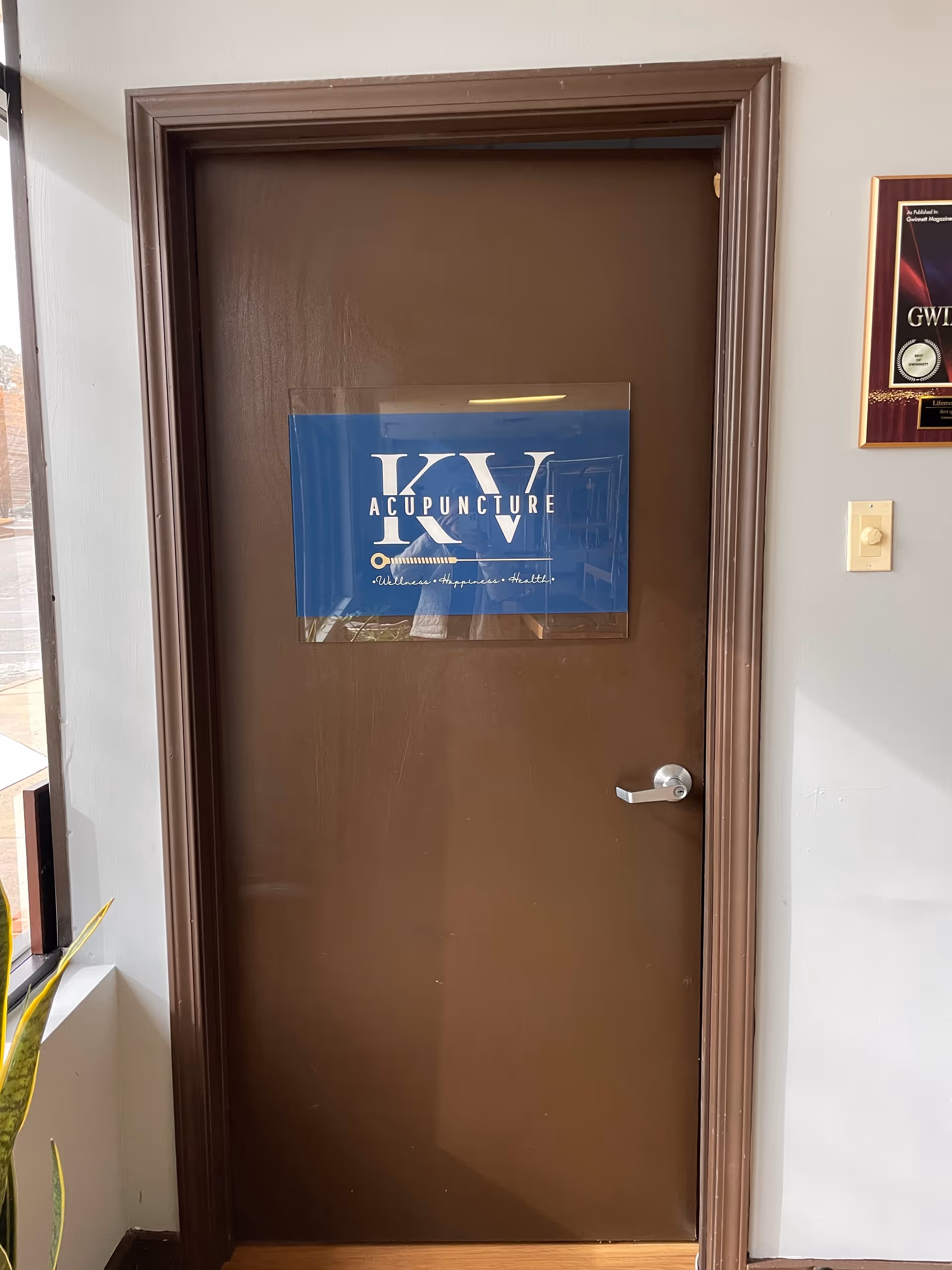 Brown interior door with a blue KV Acupuncture sign mounted at center.