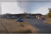 Row of single-story senior living units with a parking lot in front under a cloudy sky.