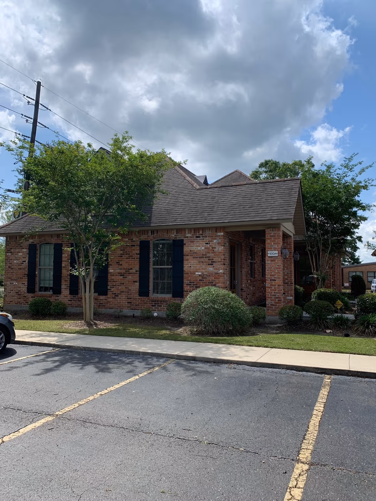 A brick senior living facility sits with trees, shrubs, and a front parking lot.