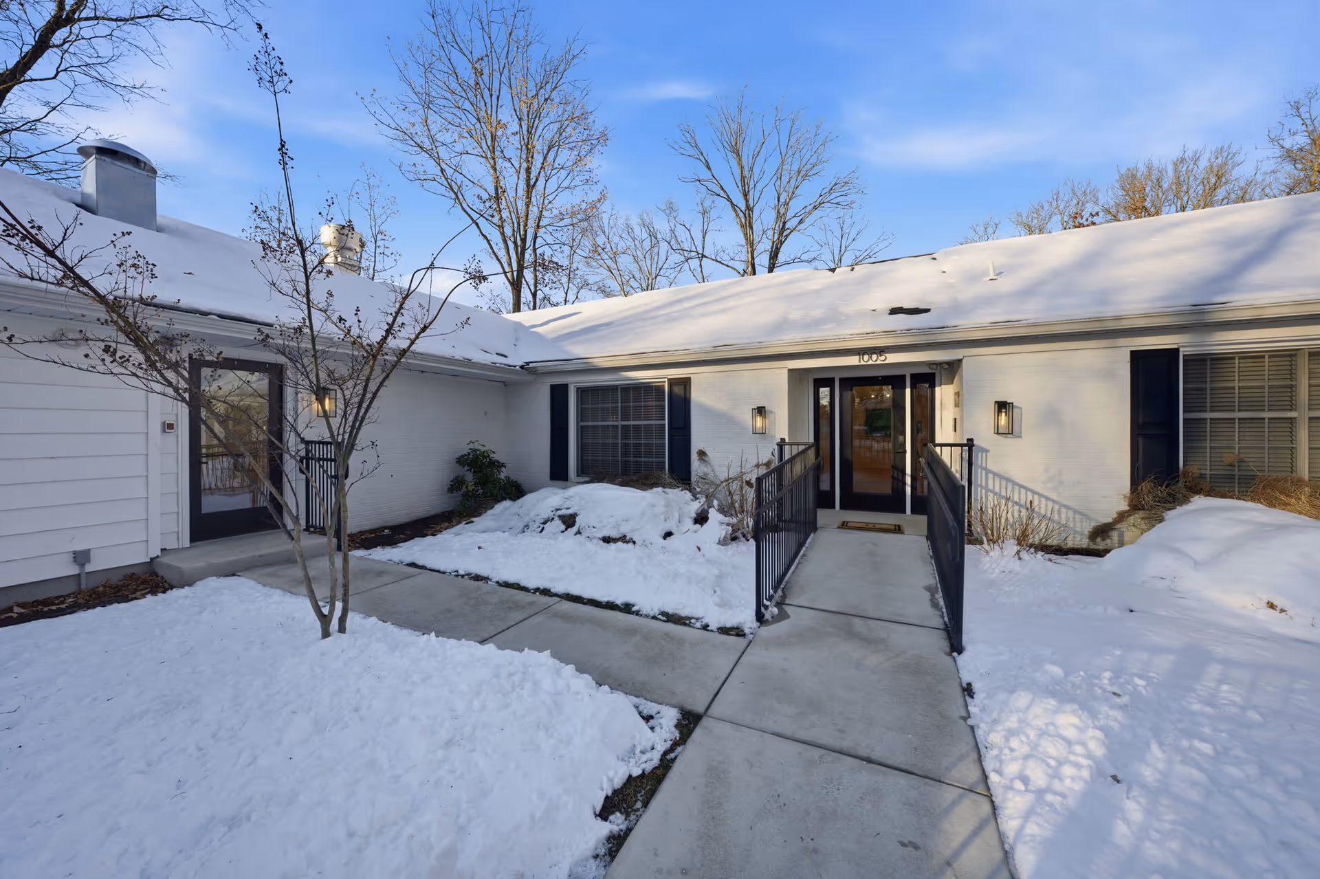 Snow-covered, single-story white facility with central entrance, walkway, and railing ramps.