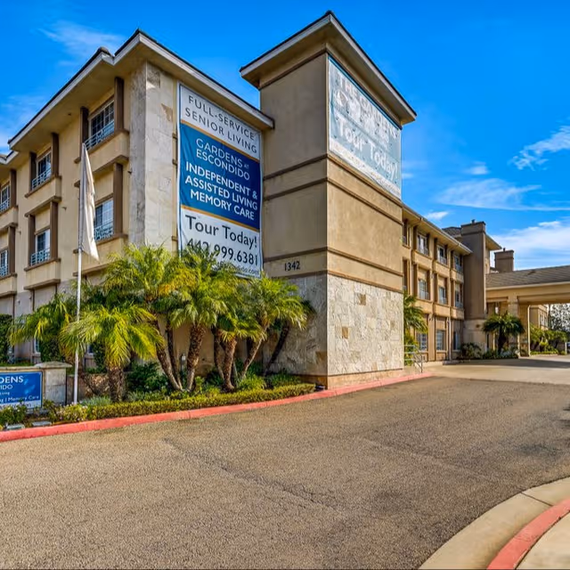 Exterior view of Gardens at Escondido with signs, palm trees, and blue sky