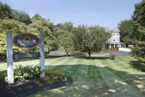 Sunrise at Gardner Park facility sign amid green lawn, trees, and the building in the background.