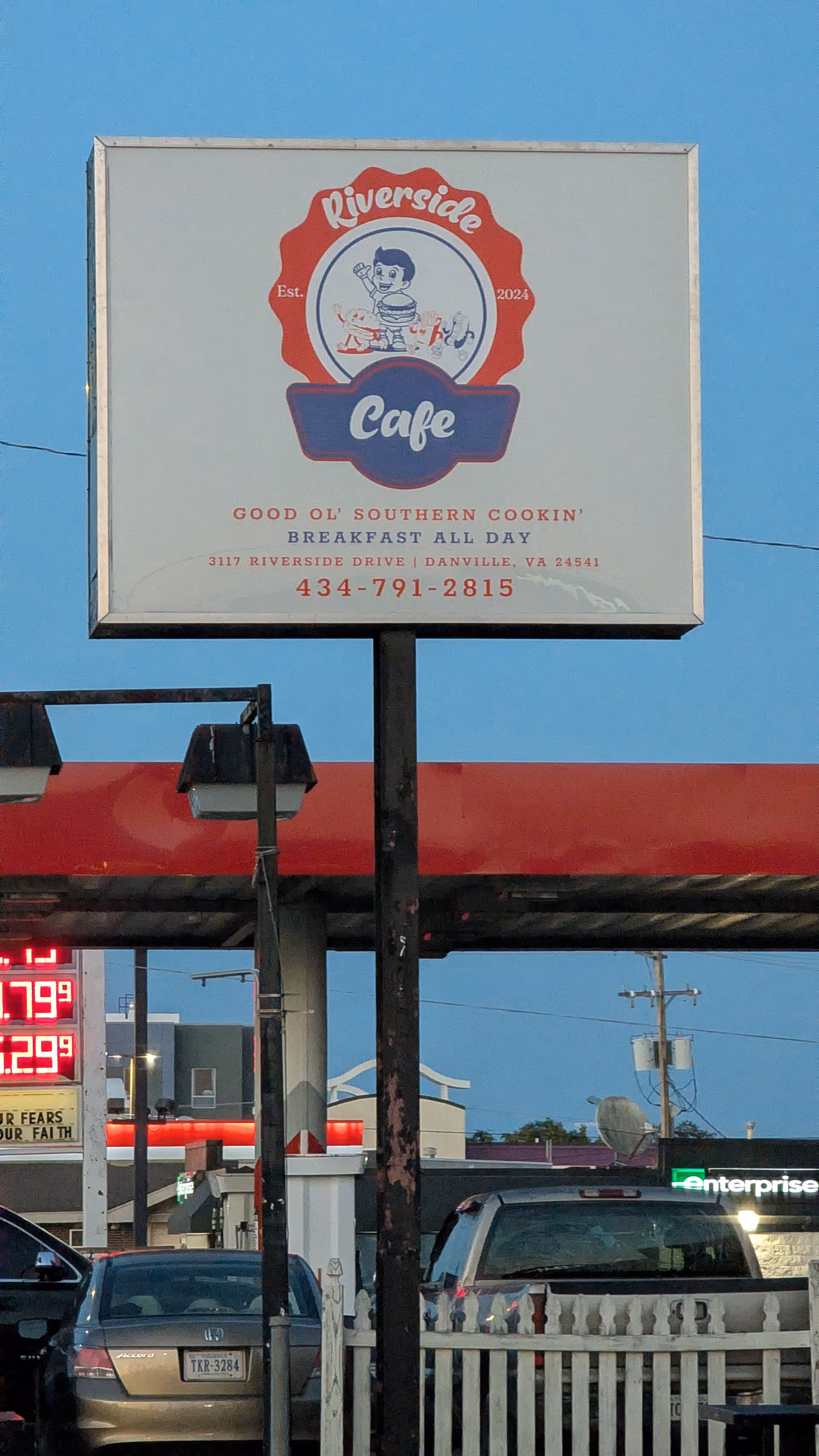 Outdoor signboard for Riverside Cafe against blue sky and nearby cars