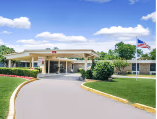 Exterior view of a senior care facility entrance with a covered drop-off, landscaping, and American flag.