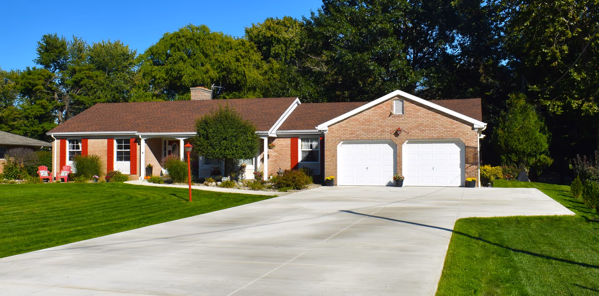 A single-story brick house with a two-car garage, spacious driveway, and green lawn.