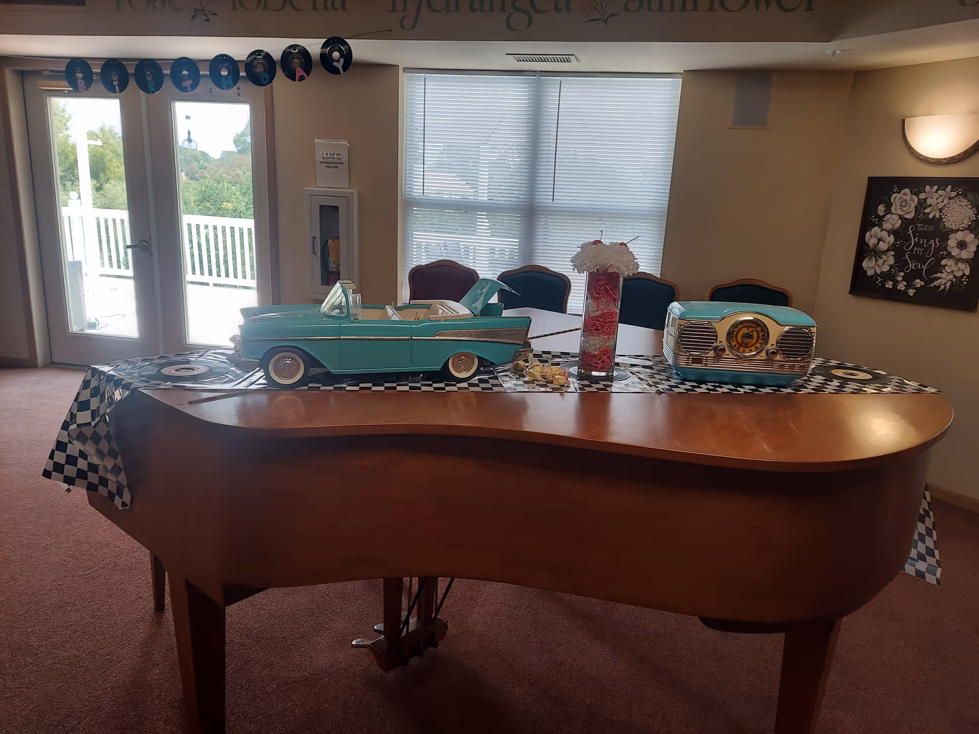 Indoor lobby with a grand piano and vintage turquoise car models on a checkered table.