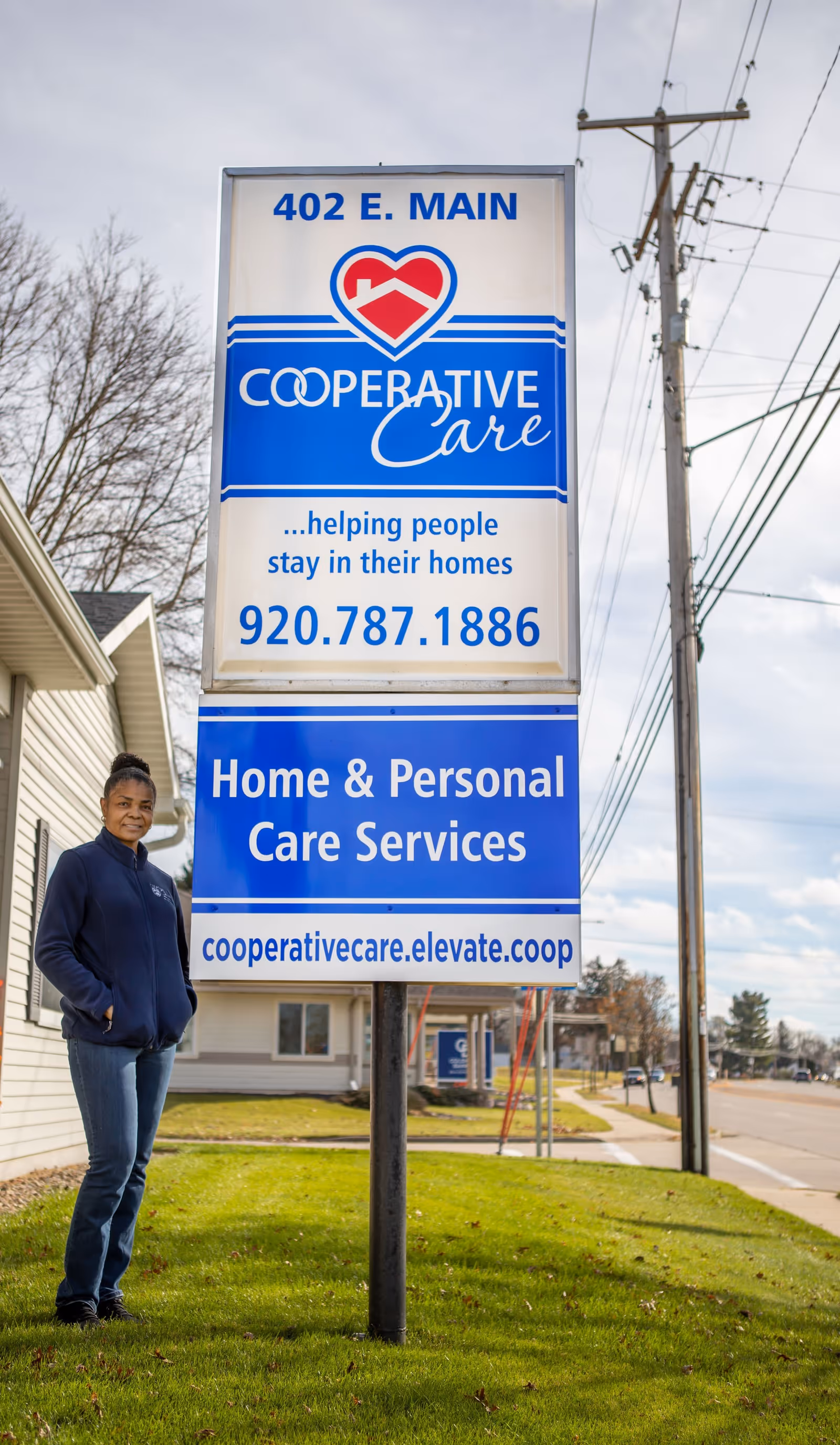 A tall blue and white Cooperative Care sign outside a building with a person nearby
