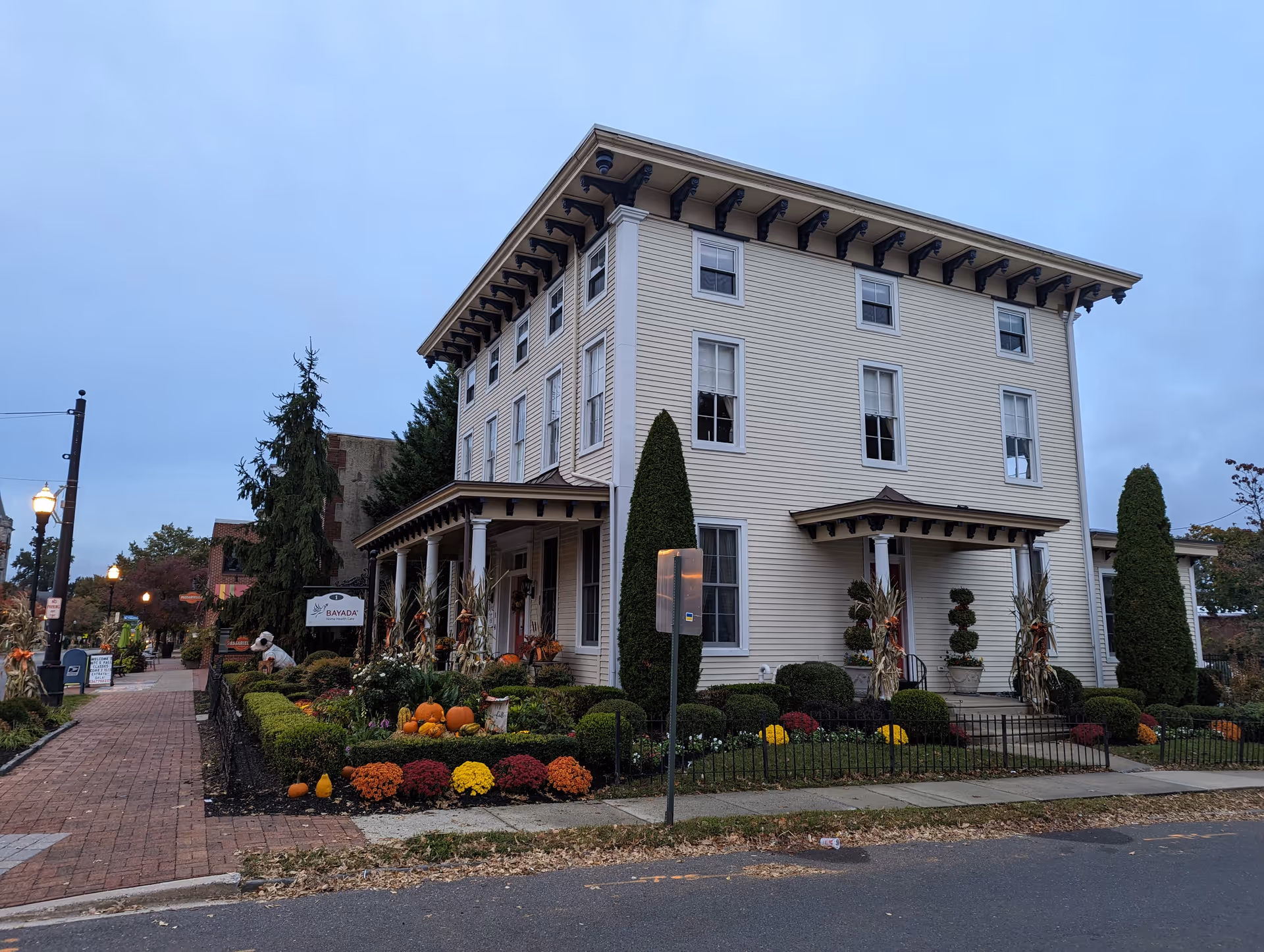 Two-story beige building with autumn landscaping, pumpkins, and decorative shrubs along the front entrance.