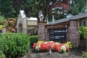 Exterior view of Marquis Autumn Hills Memory Care entrance with brick pillars and flowers.