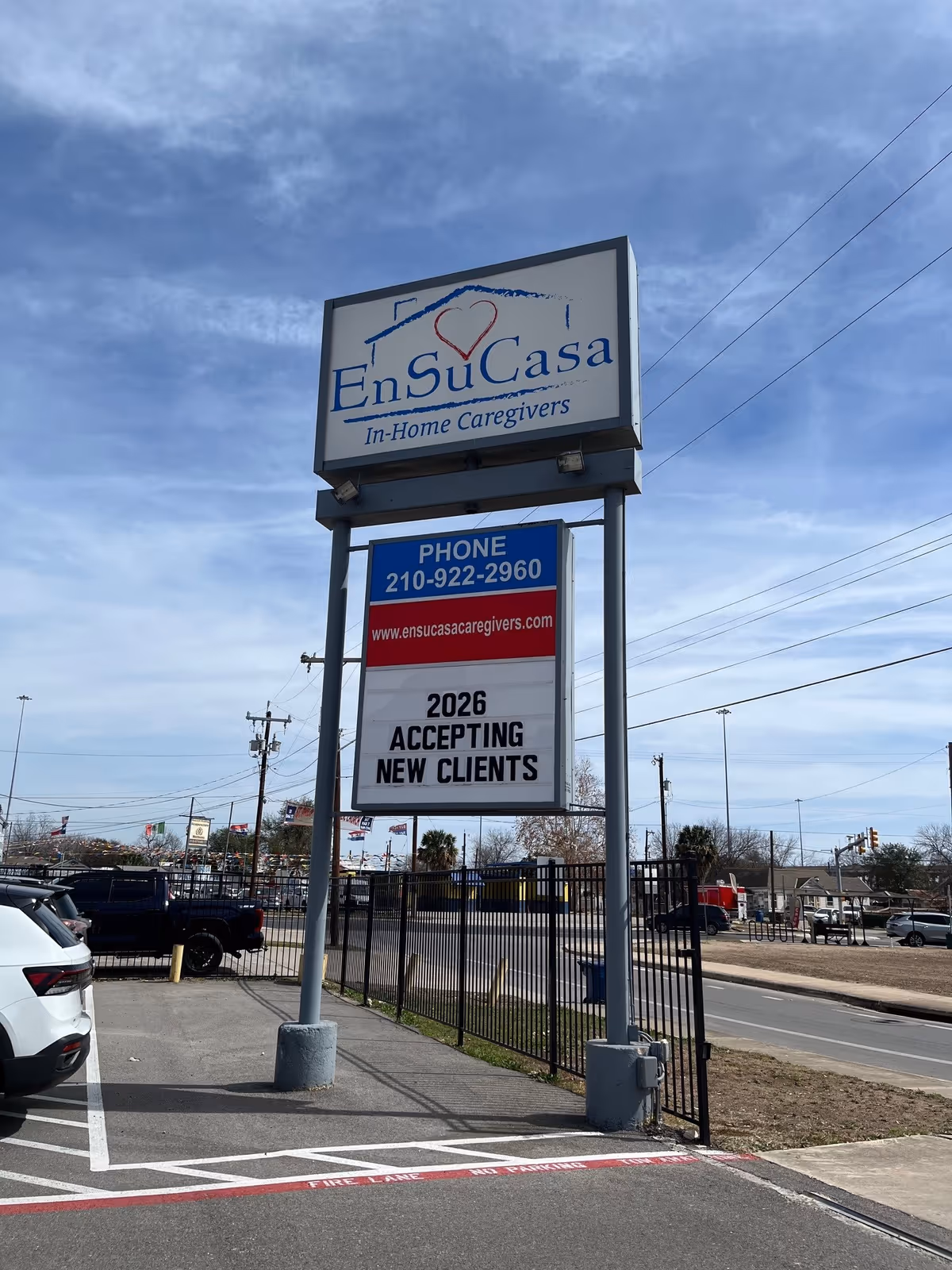 Exterior sign for En Su Casa In-Home Caregivers beside a parking lot.