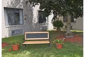 Outdoor lawn area with a wooden bench and potted plants beside a beige building.