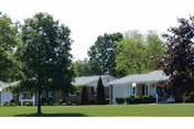 Single-story senior living complex with green lawns, trees, and a driveway along the front.