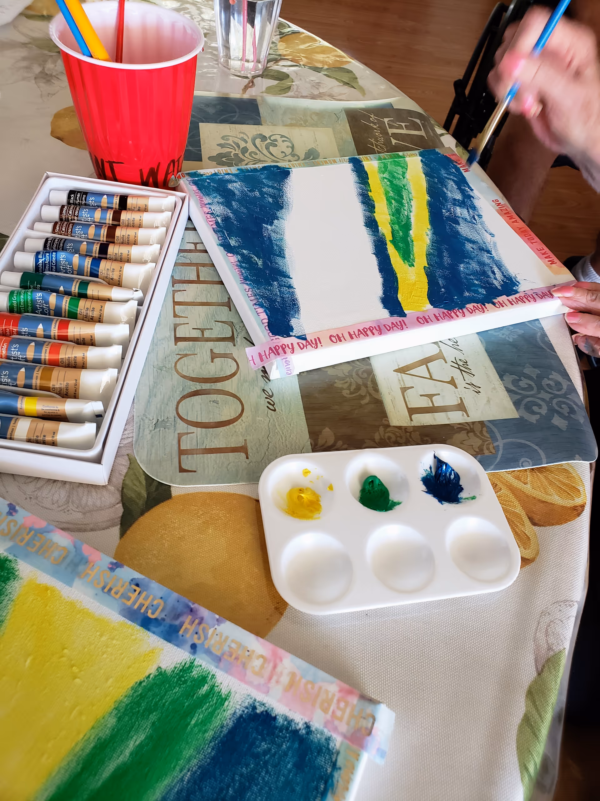 Art supplies and a painting in progress on a table with paints and brushes.