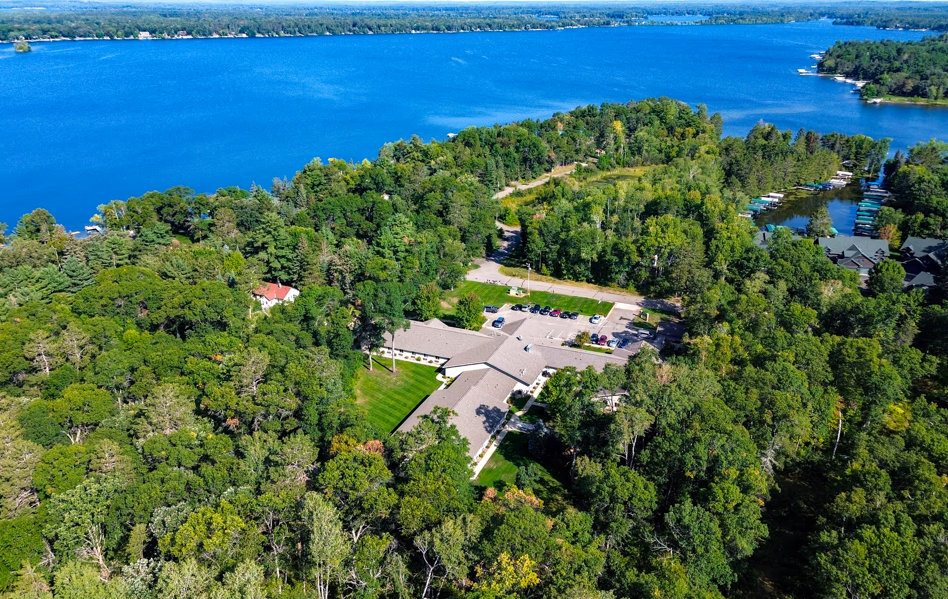 Aerial view of a single-story senior living facility surrounded by dense trees on the shore of a large blue lake.
