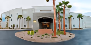 Front entrance of a white curved senior living building with a circular driveway, desert landscaping, and palm trees.