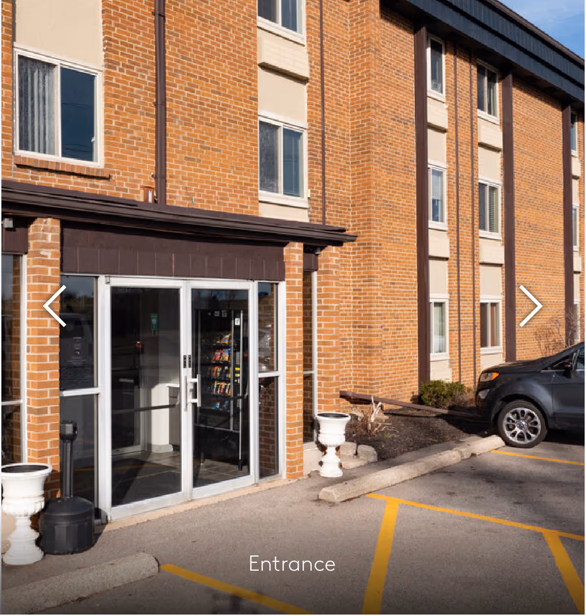 Brick exterior of a senior living building with glass entrance doors and a parked car.