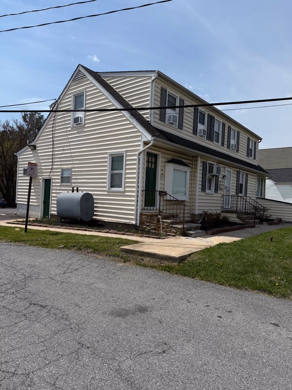 Two-story beige clapboard building with a green door, stairs, and window air conditioners.