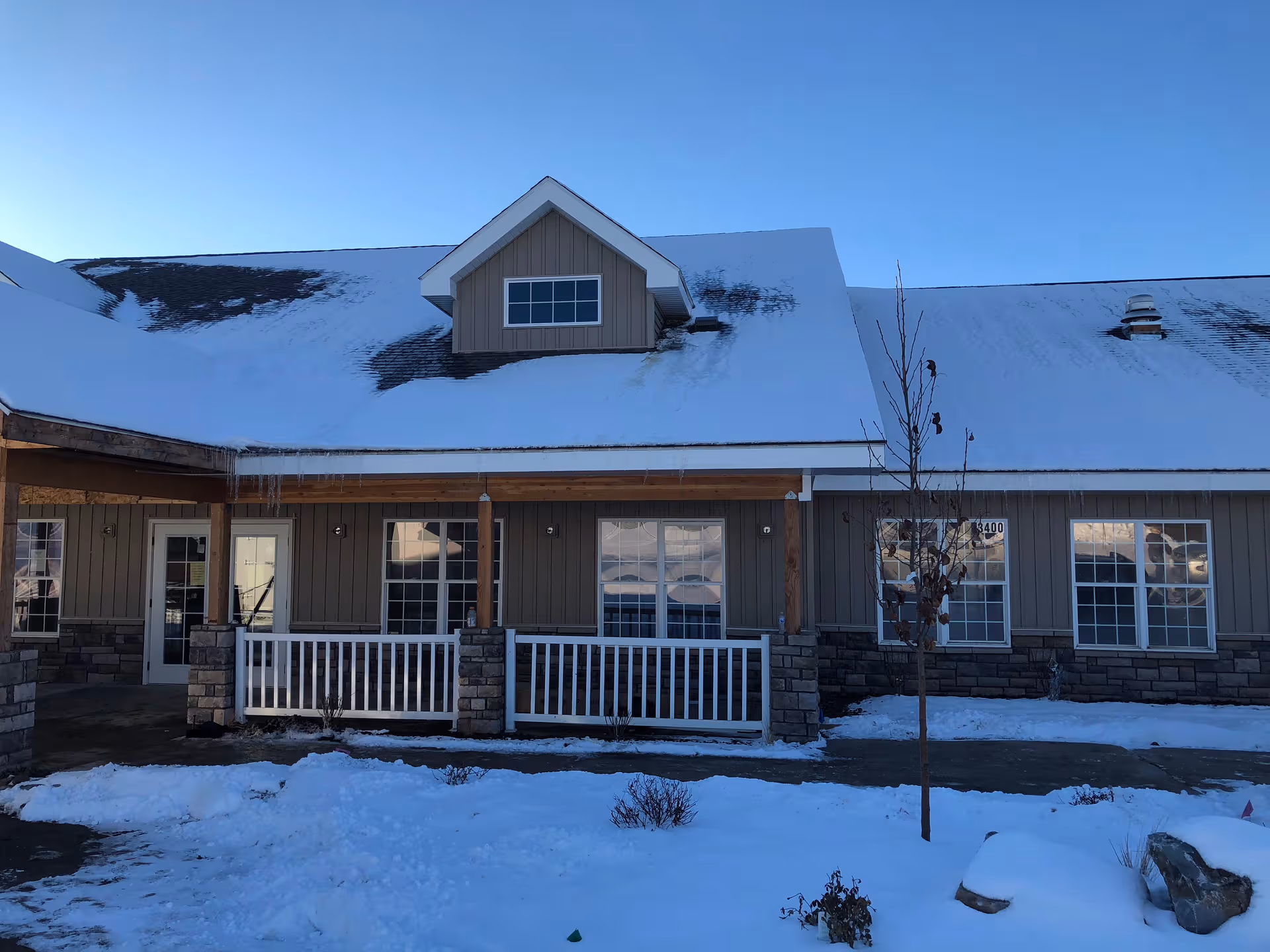 Snow covers the front of a single-story assisted living building with a wooden porch.