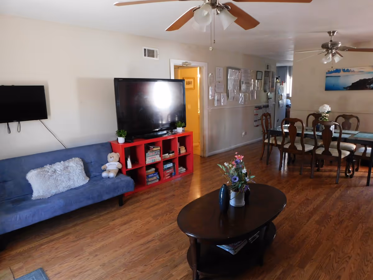 Open living area with blue sofa, TV, red shelf, and dining table in a communal room.