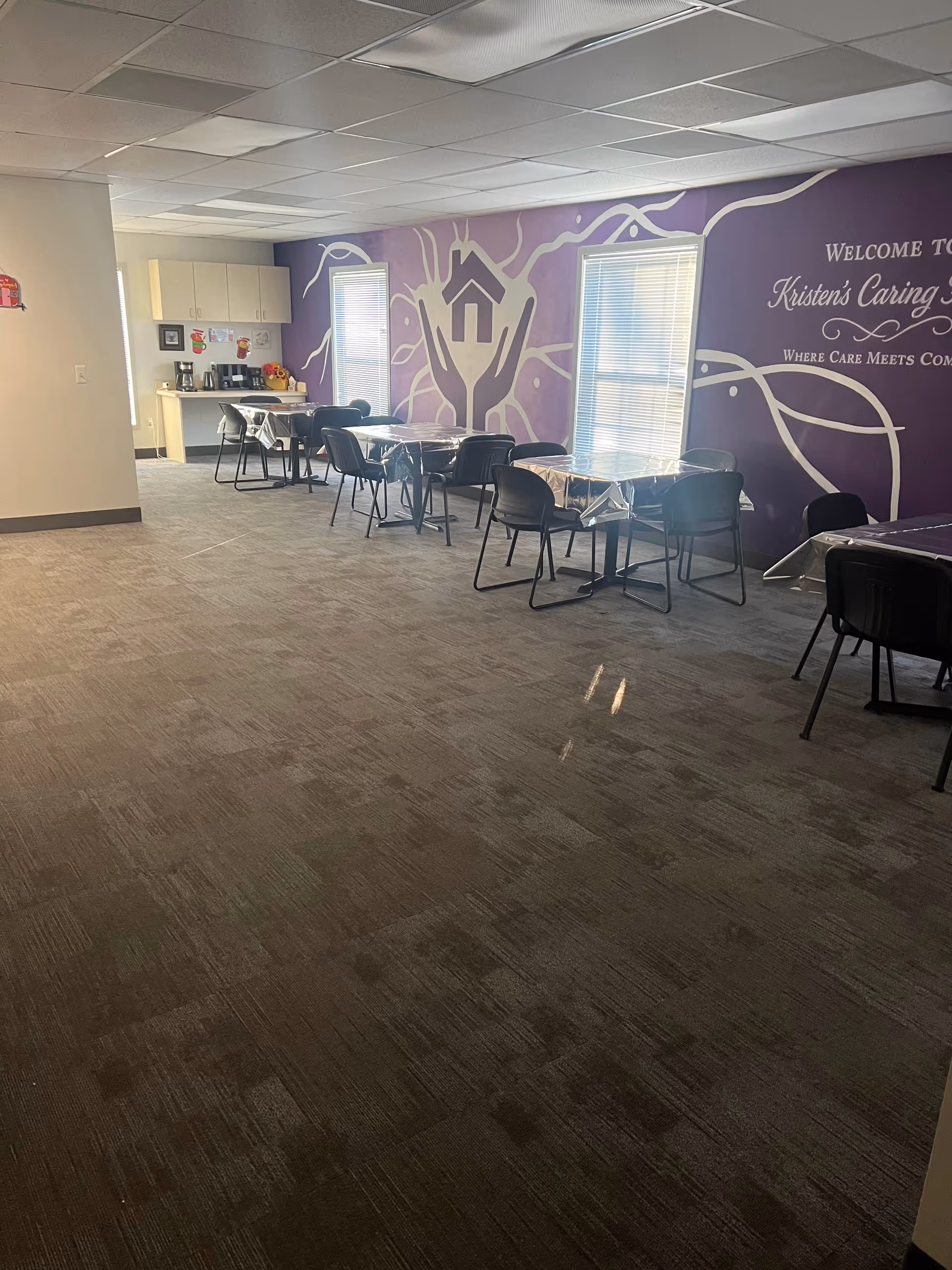 Dining room with plastic-covered tables, black chairs, and a purple wall mural.