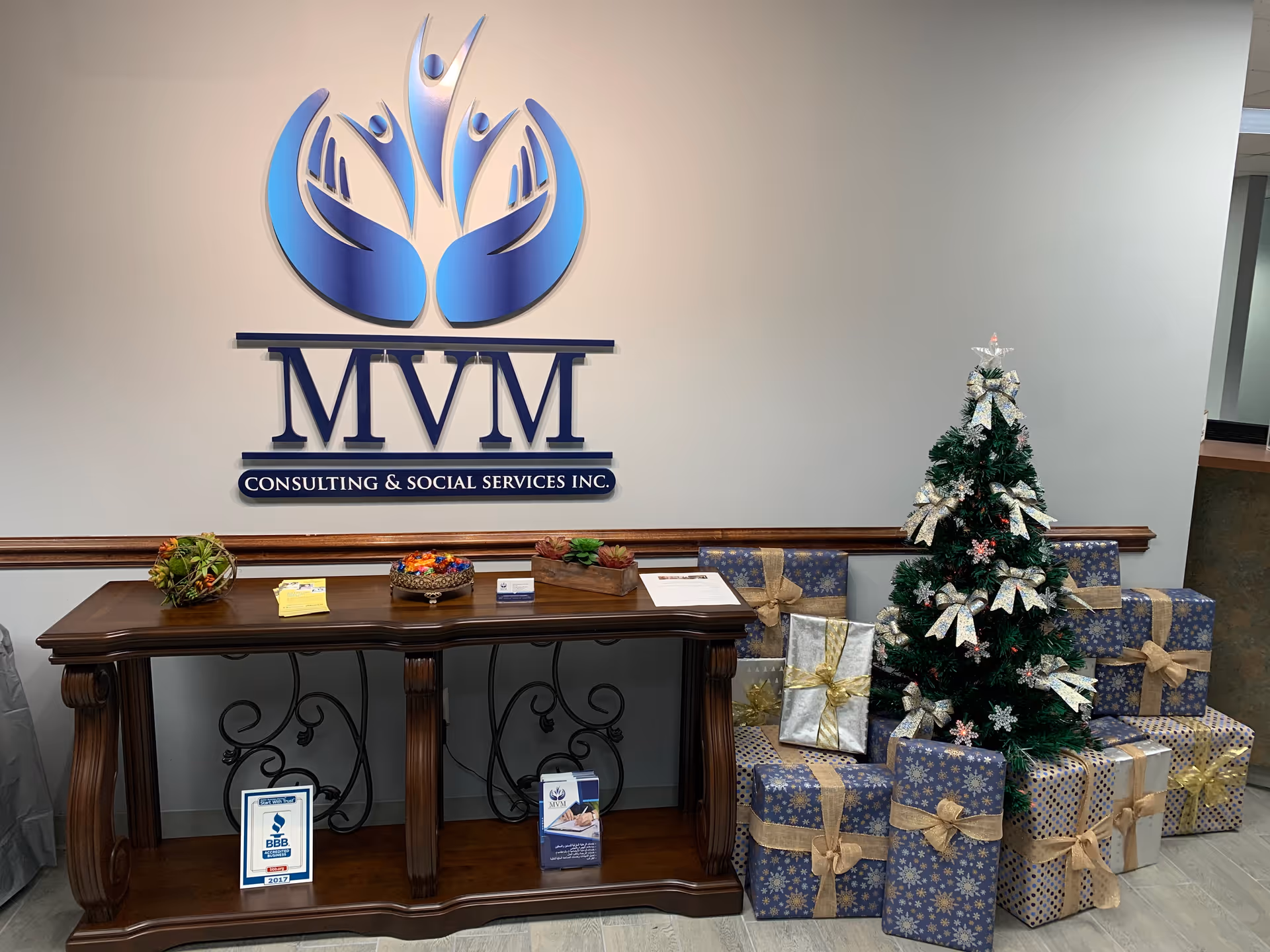 Lobby area with MVM Consulting logo on wall, decorative desk, Christmas tree and wrapped gifts.