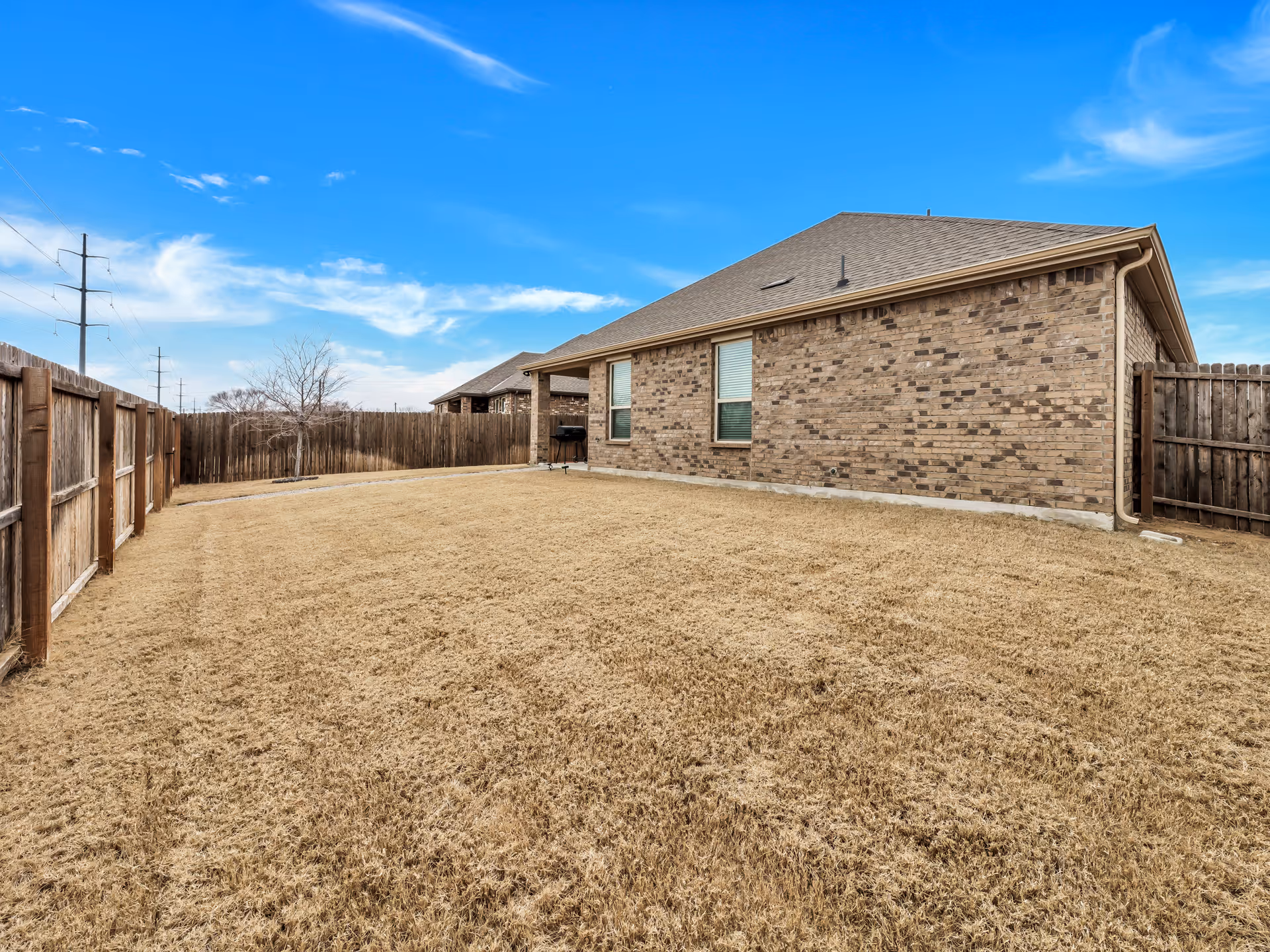 Single-story brick building with a large fenced yard and clear blue sky.