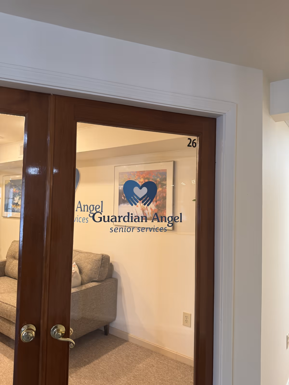 Glass door entrance with Guardian Angel Senior Services logo and a beige seating area inside.