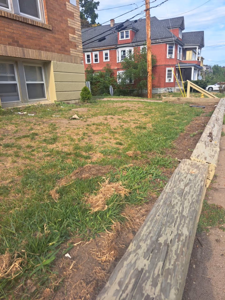 Exterior view of a brick building with a grassy yard and weathered wooden barrier.