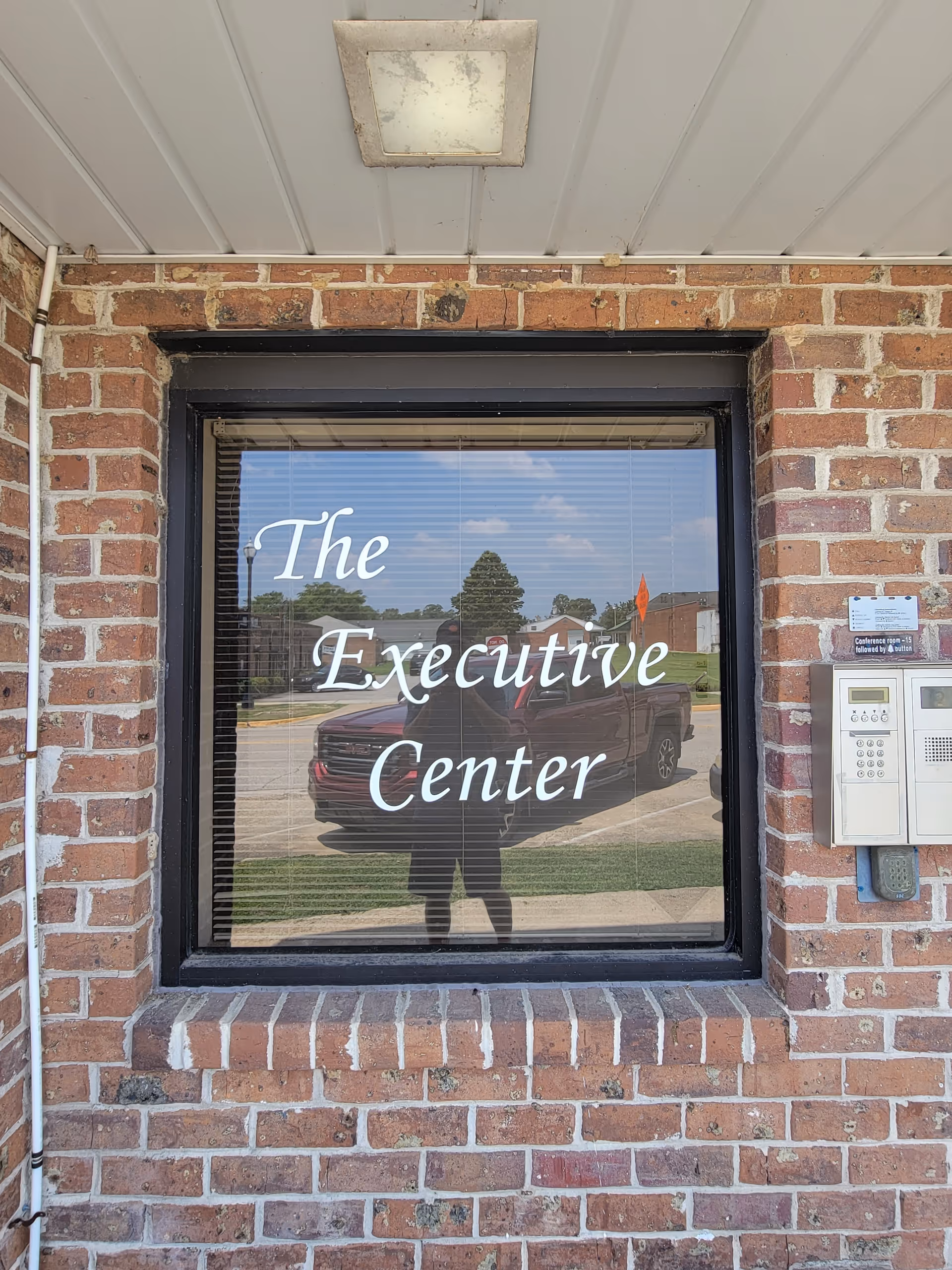 Brick building exterior with a window sign reading The Executive Center and a reflected person.
