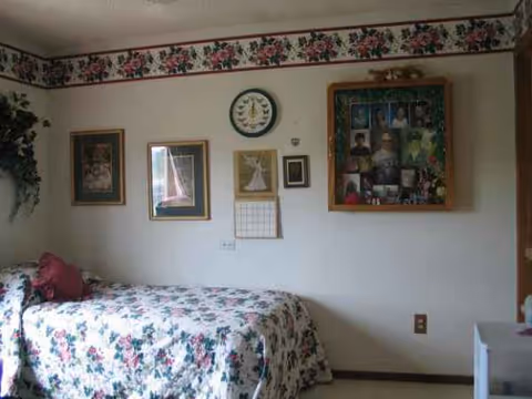 A floral-patterned bed sits in a small room with framed wall pictures.