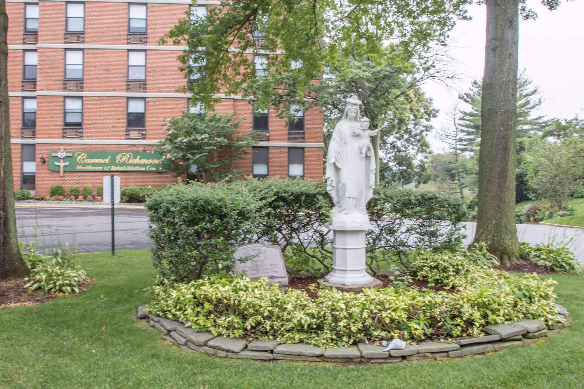 Brick Carmel Richmond Healthcare and Rehab Center exterior with statue in circular flower bed.